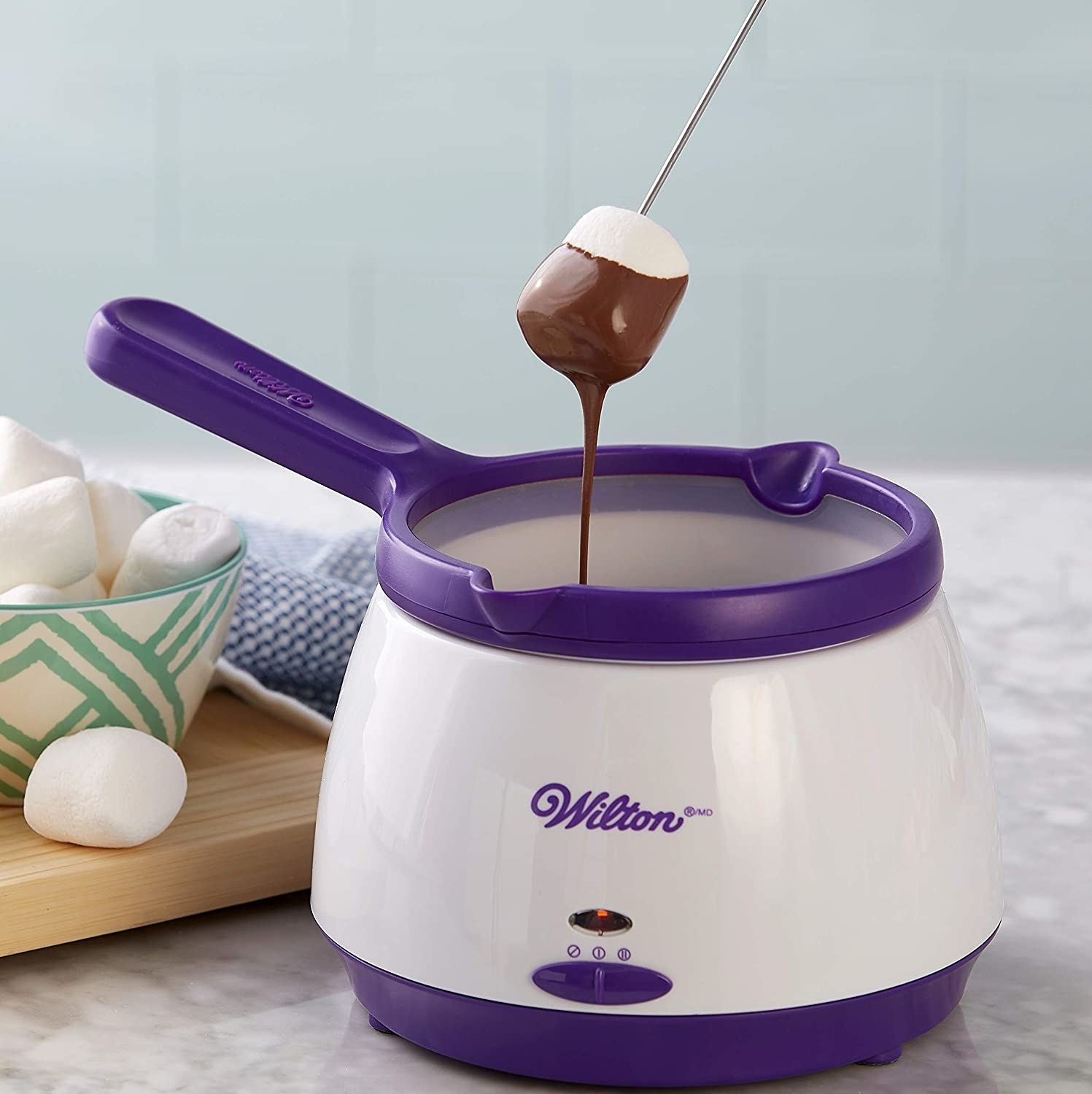 A person dipping a marshmallow into the pot filled with chocolate