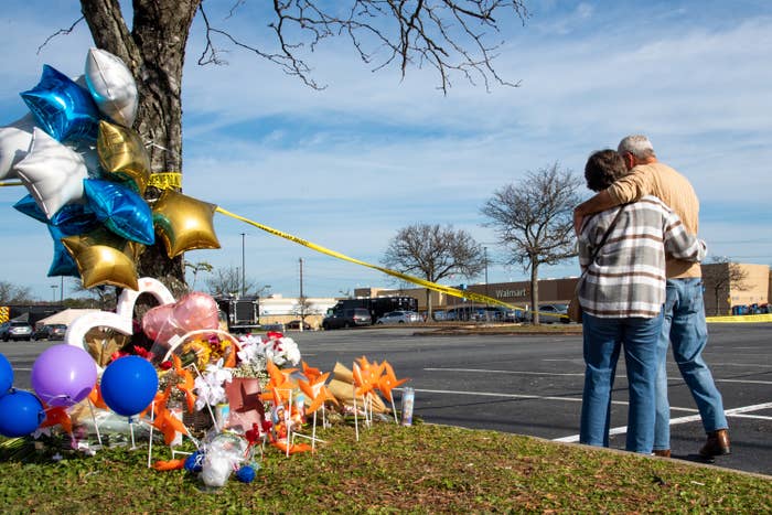 Two people hug next to a vigil site with police tape