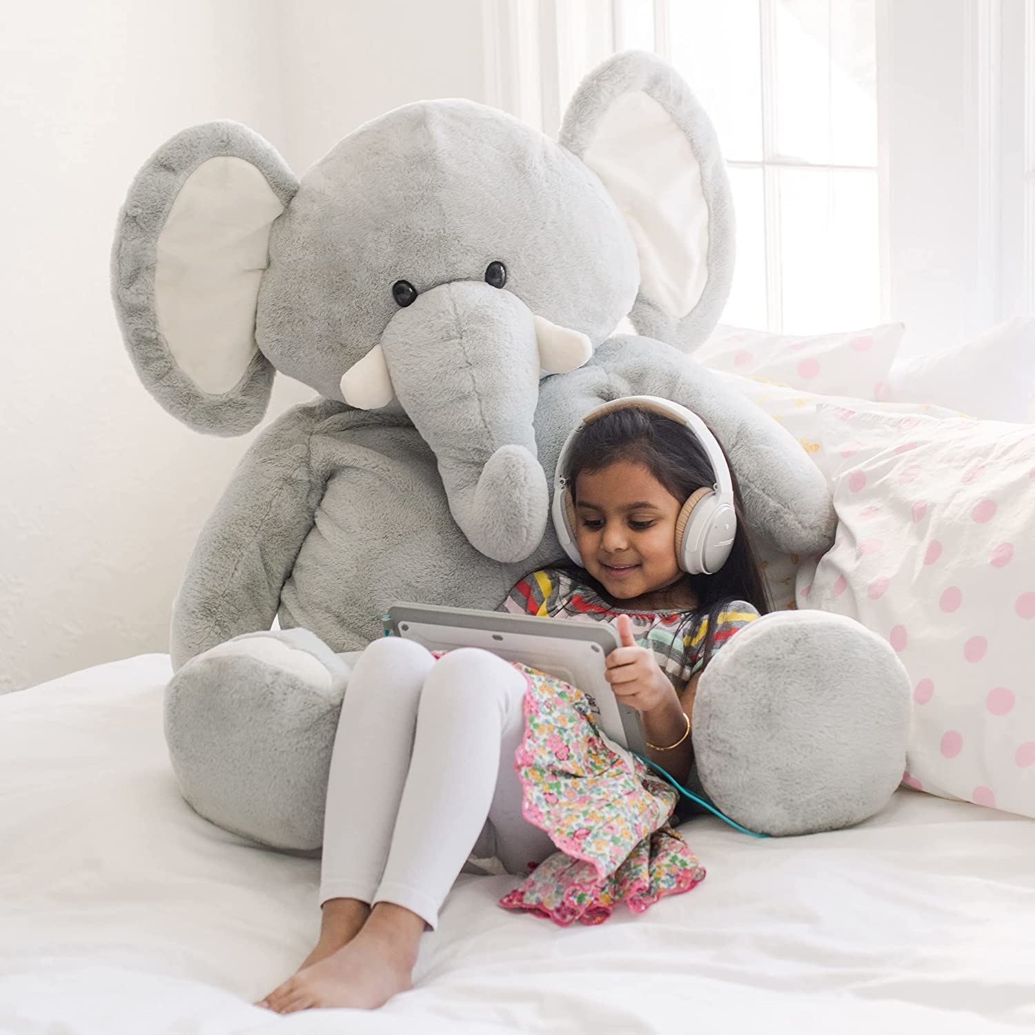 Child model being cuddled by large gray stuffed elephant toy