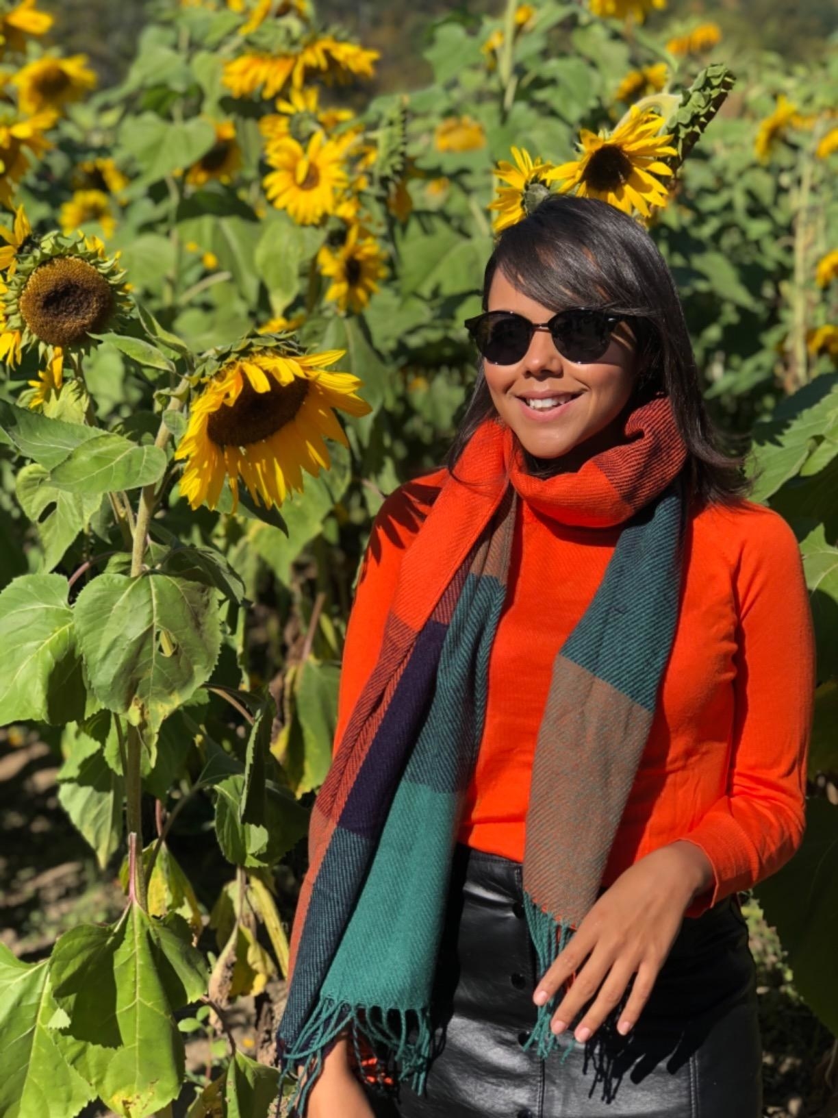 Reviewer standing outside by sunflowers in red sweater, black bottoms, and the blue and red scarf tied around neck
