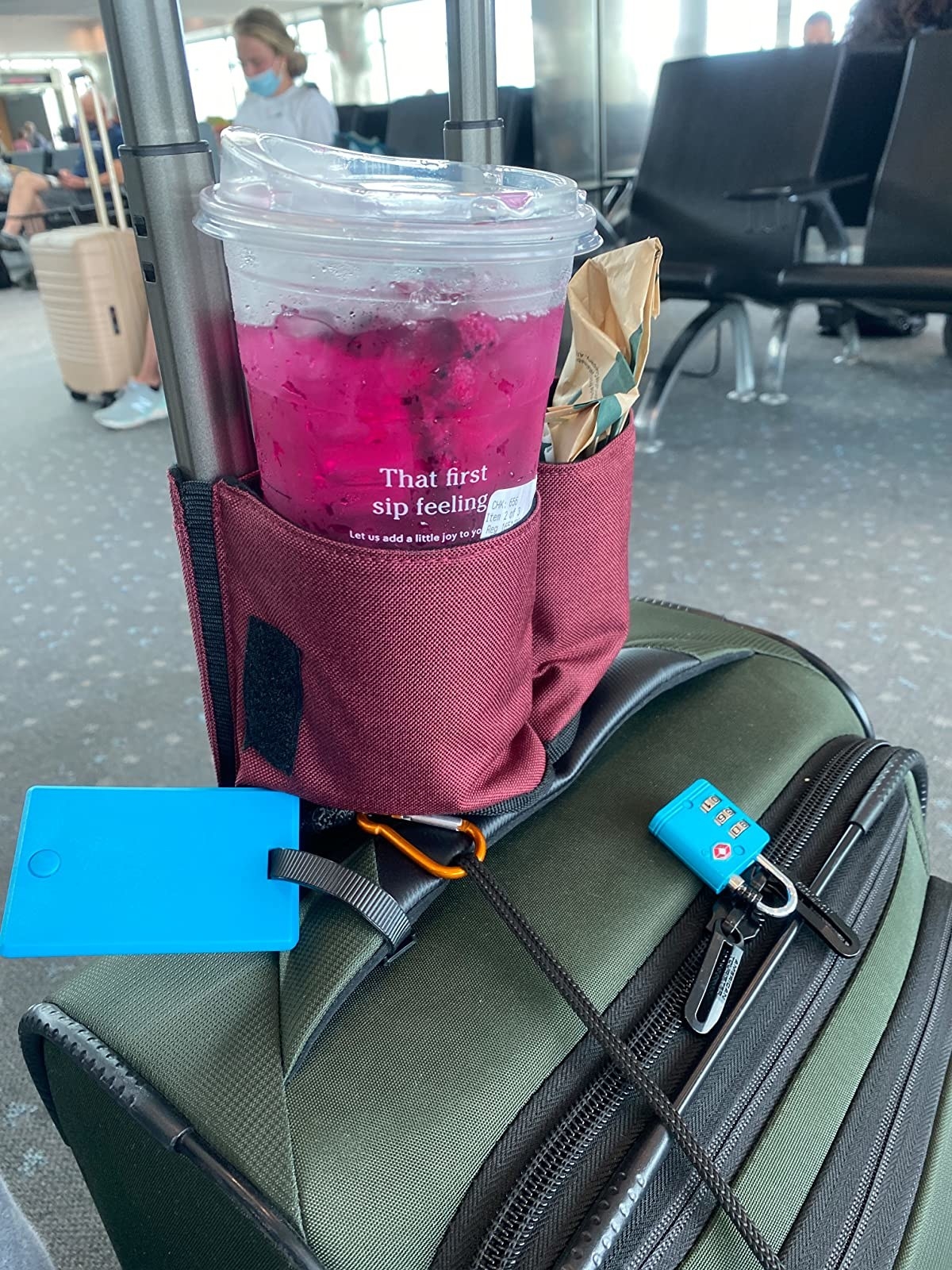 reviewer photo of a burgundy-colored caddy mounted on a rolling suitcase and holding an iced beverage and a snack