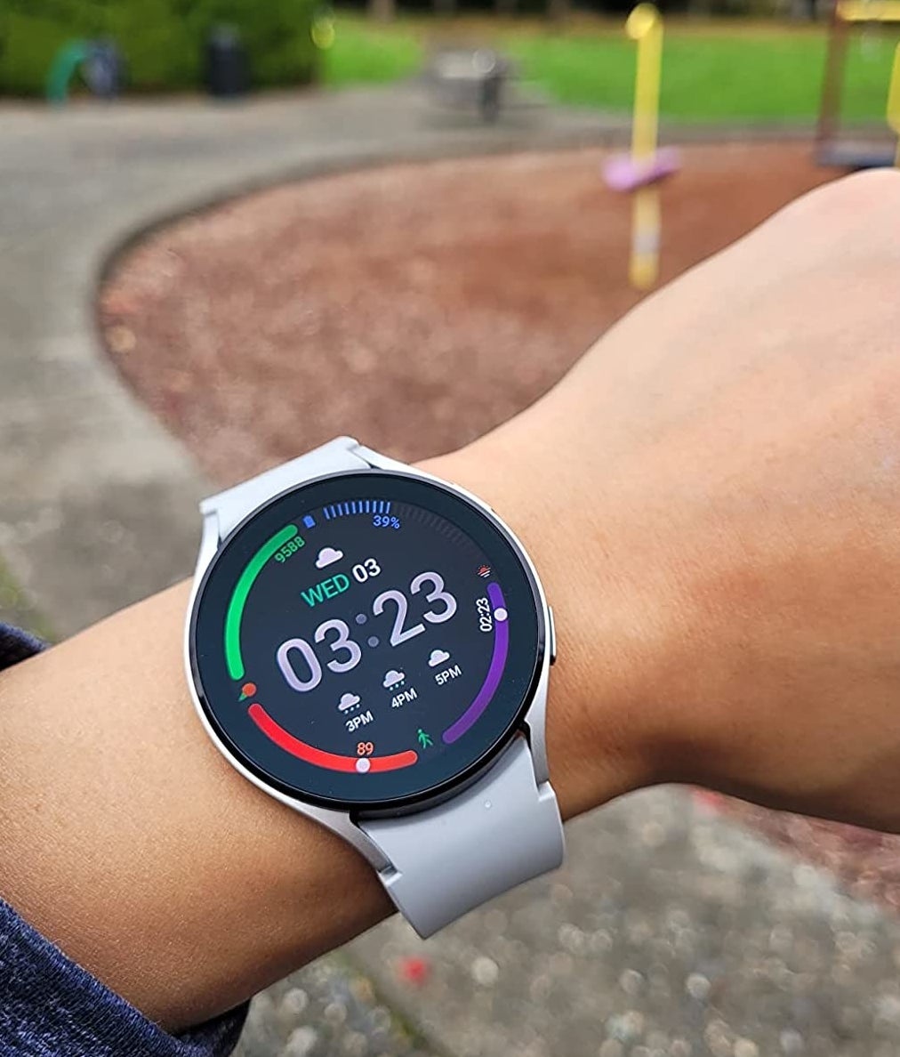 Reviewer wearing white smartwatch with black display screen showing the time, weather, fitness tracker