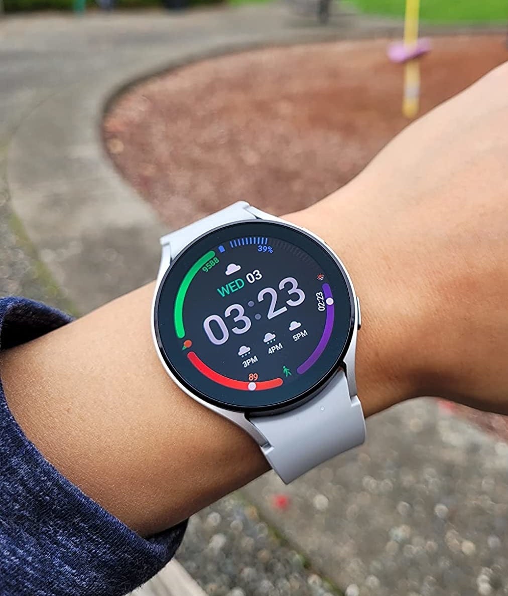 Reviewer wearing white smartwatch with black display screen showing the time, weather, fitness tracker