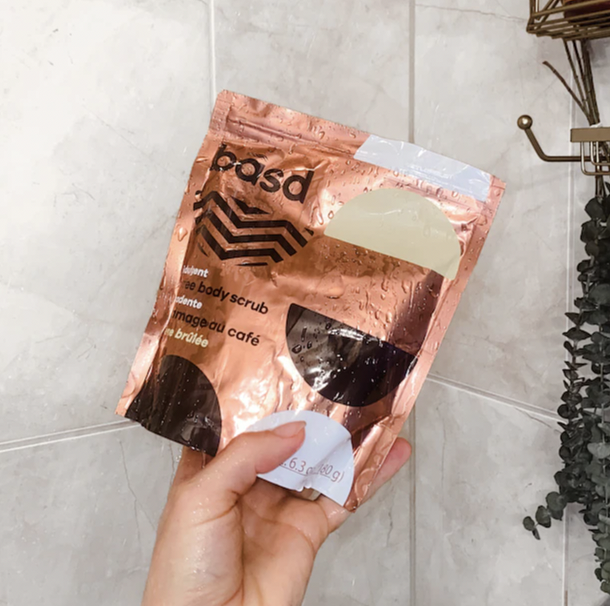 a person holding up a bag of the coffee scrub in their bathroom