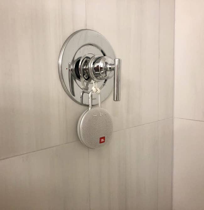 Waterproof speaker hangs from a facuet on a bathroom wall 