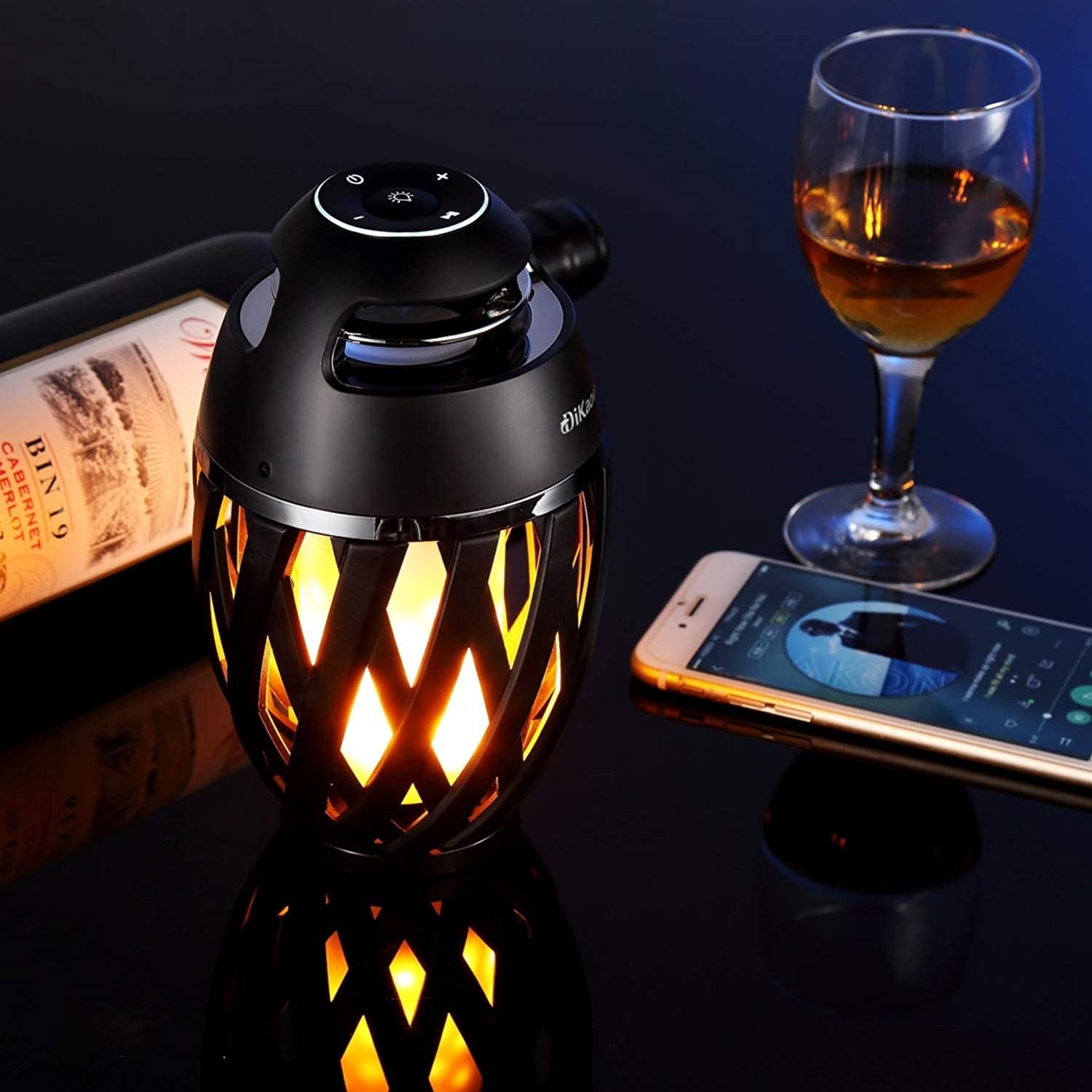the flickering flame speaker next to a phone and a glass of wine