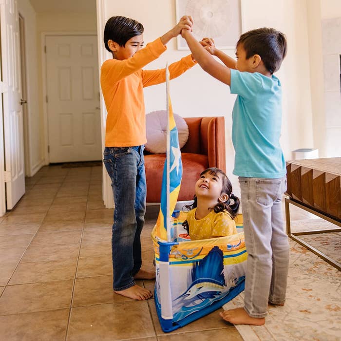 Three kids playing with the boat set in a living room