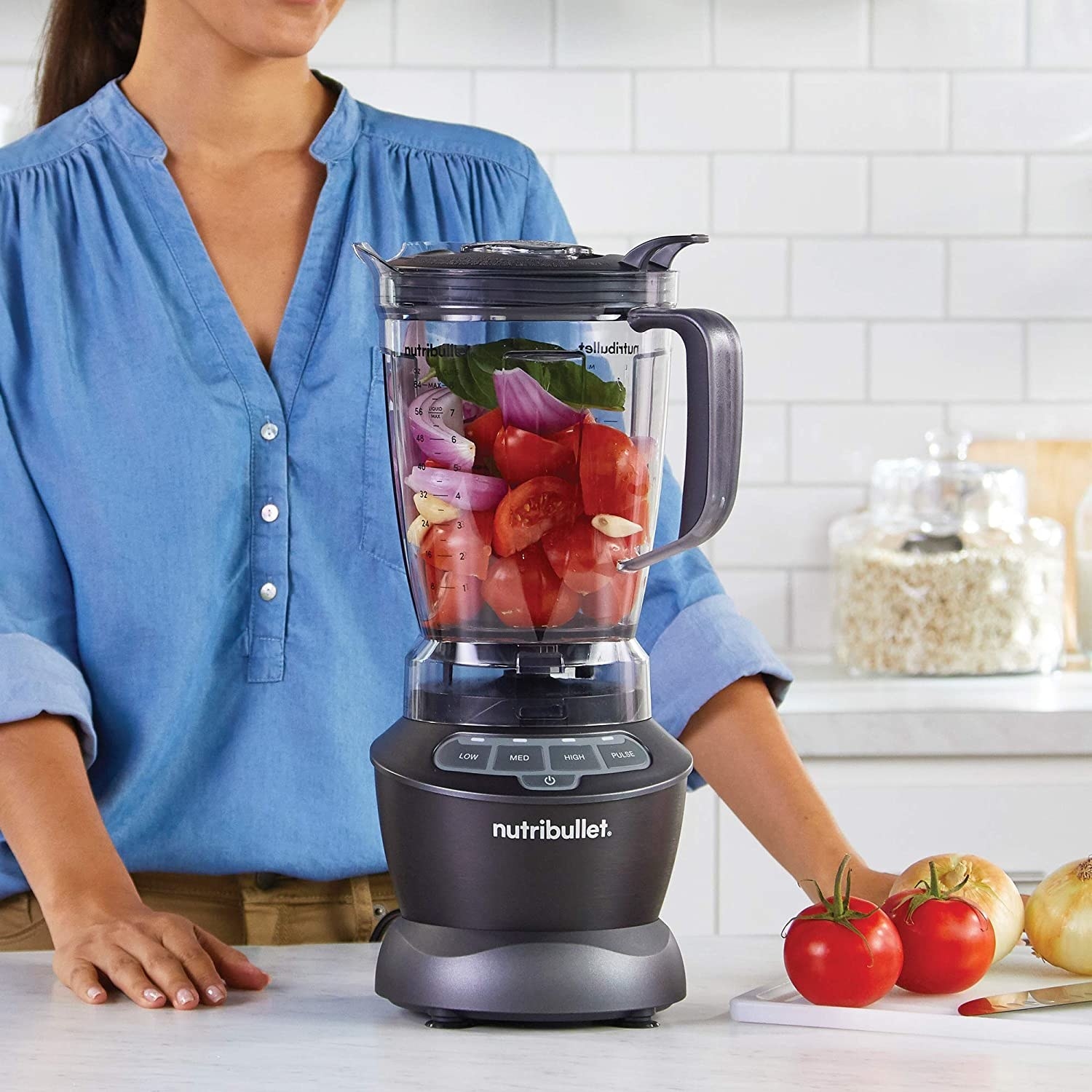 A person standing behind a blender filled with veggies