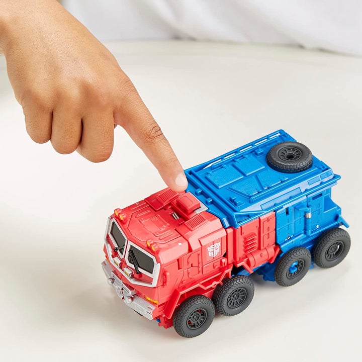 Child model's finger pointing to transforming mechanism on red and blue truck toy