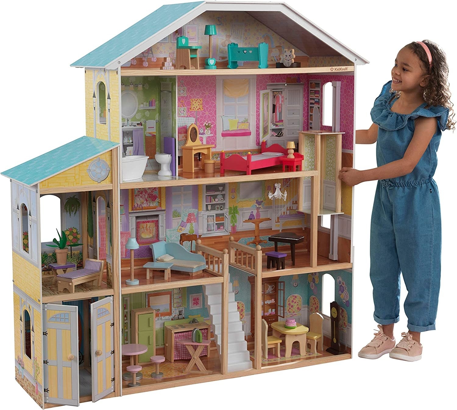 A kid standing next to the doll house playing with the elevator inside