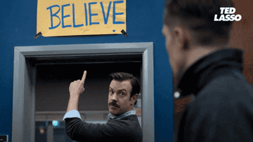Ted Lasso pointing to a sign that says believe