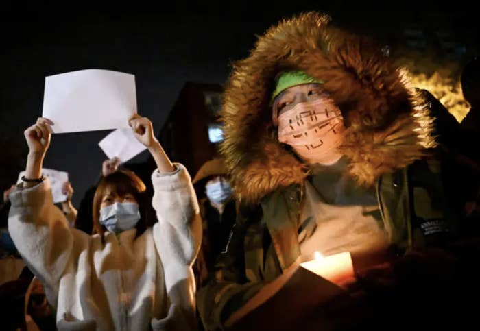 two people in winter clothing hold up a blank piece of paper and candle, respectively