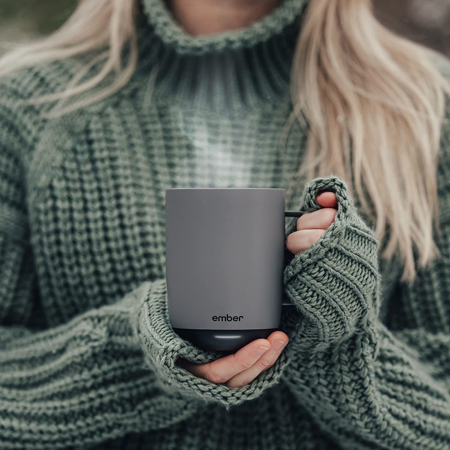 A person wearing a cozy sweater and holding the mug