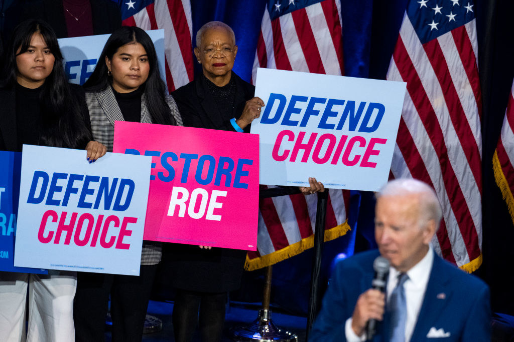 People carrying signs that say, &quot;Defend Choice&quot; behind Joe Biden
