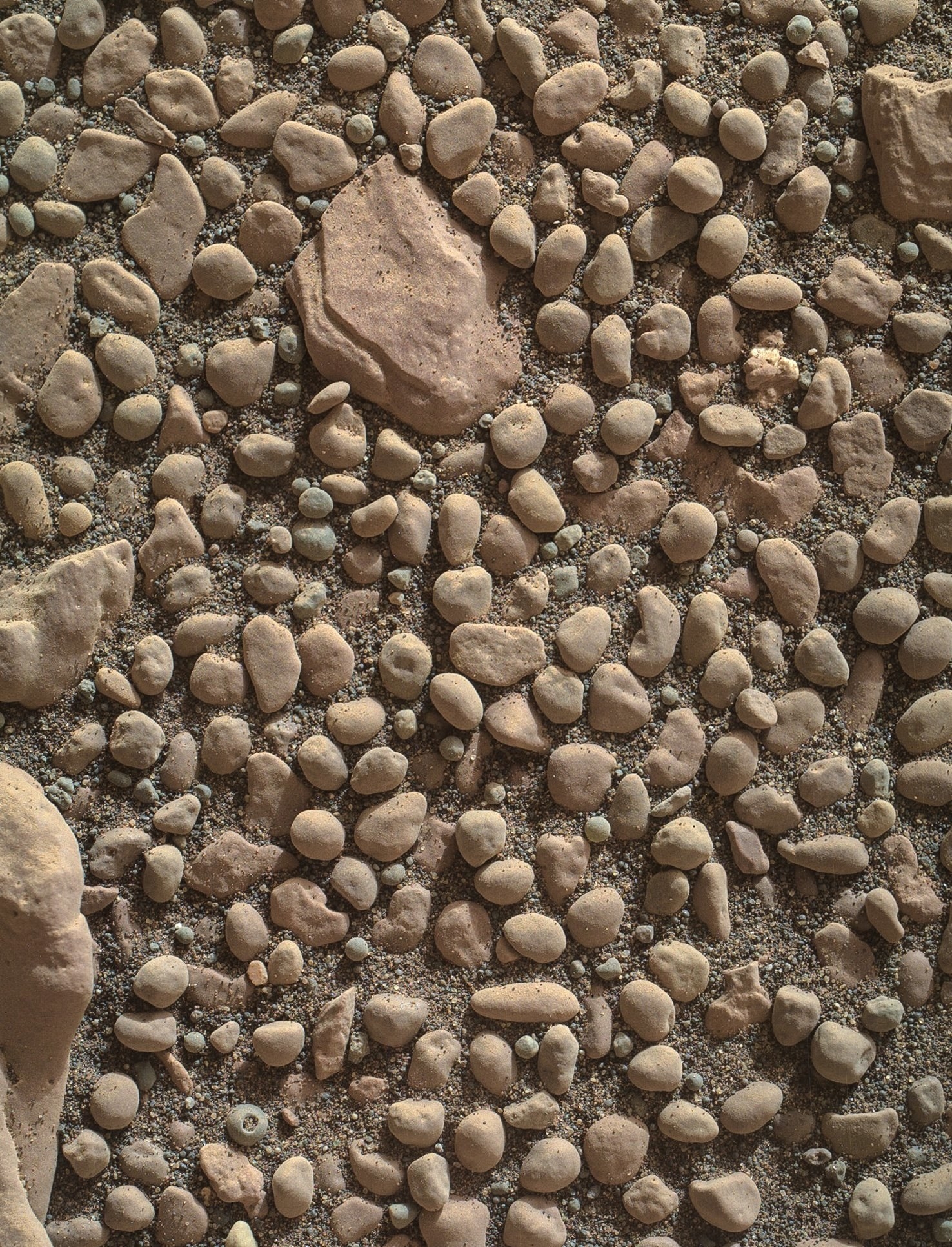 Many large pebbles and stones on a sandy surface