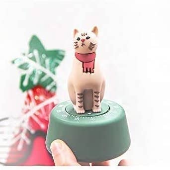 a hand holding up a green timer that has a cat wearing a red scarf on top of it