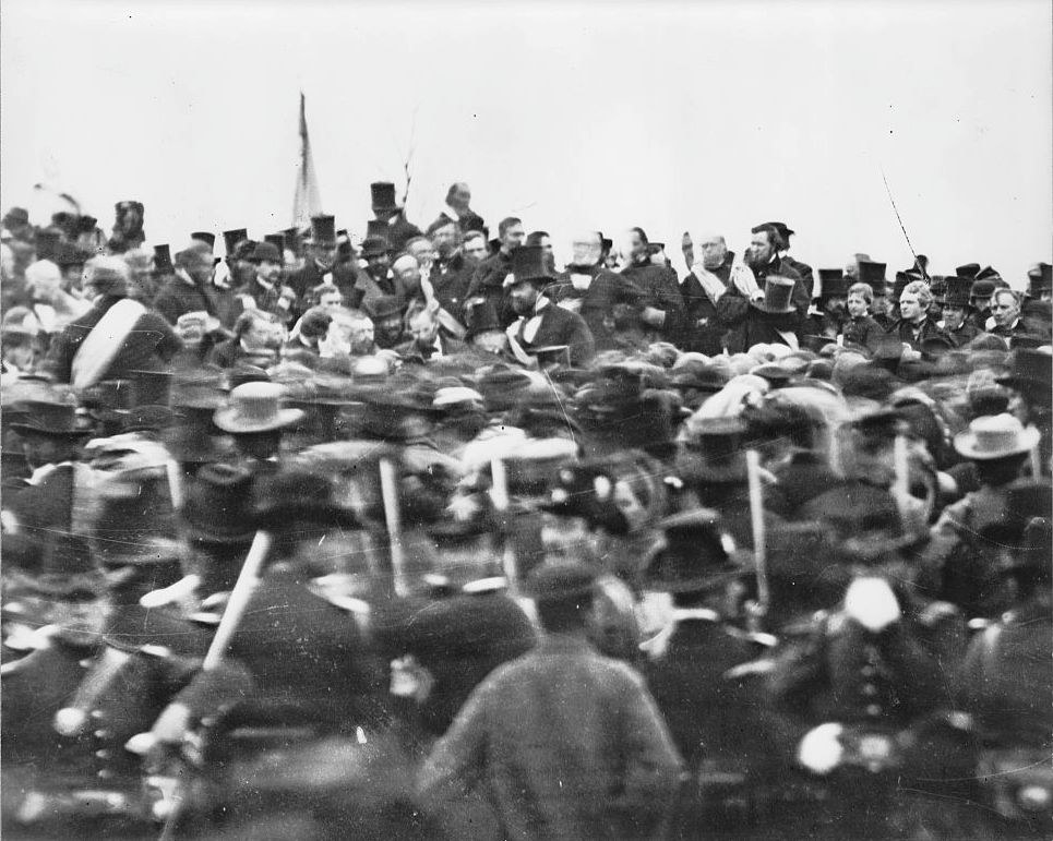 A black-and-white photo of a crowd, with many in it wearing top hats, with a man who appears to be Abe without a hat at the top right