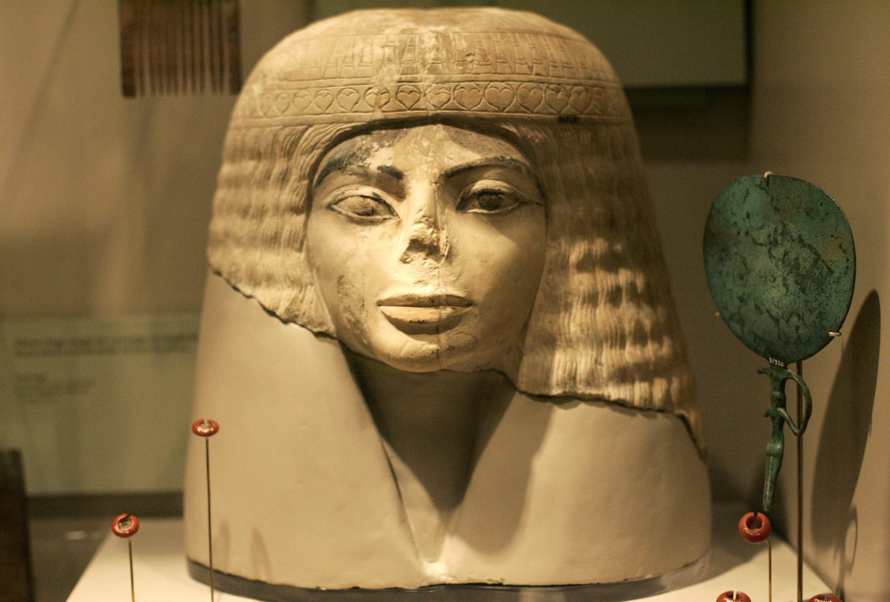 The head of an Egyptian statue with a damaged nose and large eyes with eyeliner