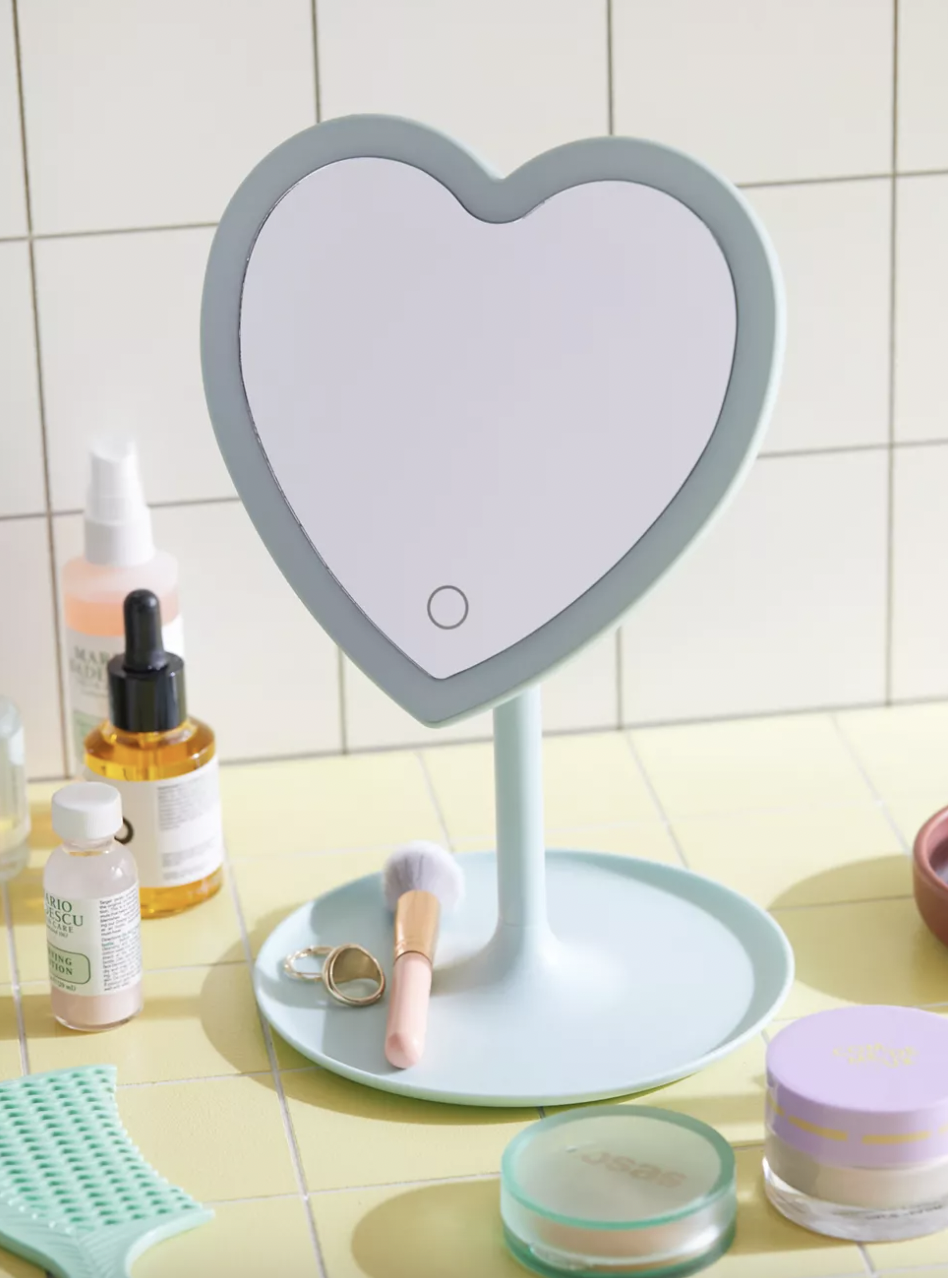 a heart shaped backlit vanity mirror with a small tray at the base