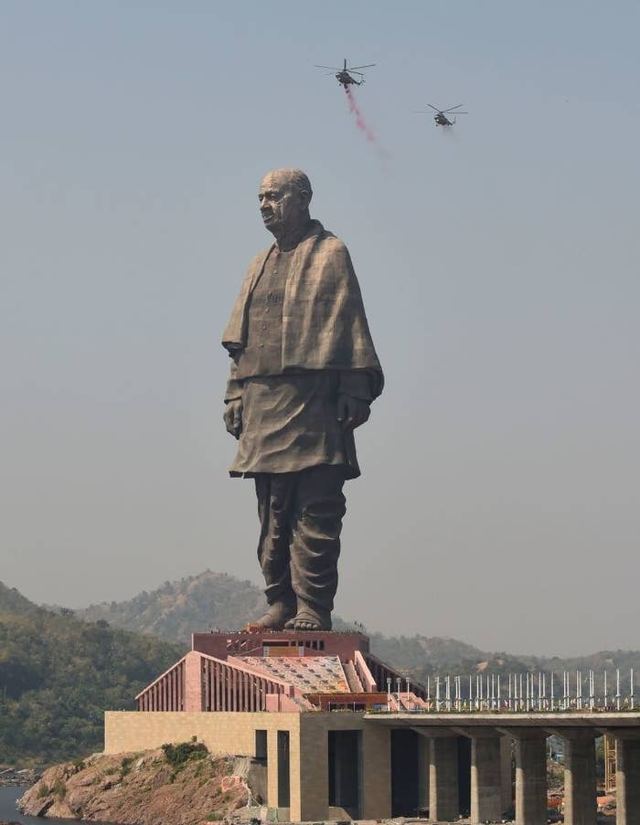 The statue of a barefoot man wearing loose pants and a shawl appears on top of a roof