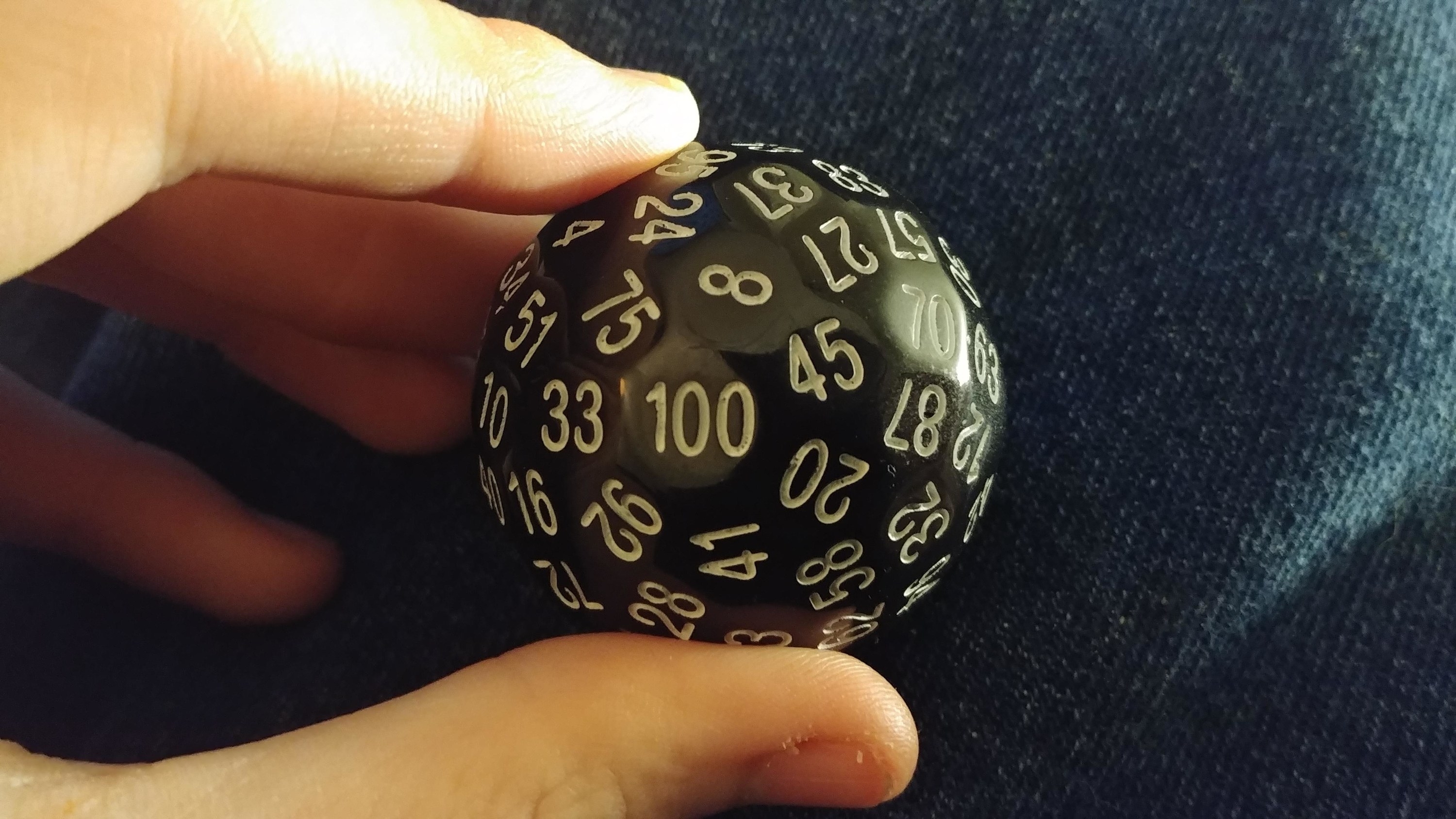 A circular die with many numbers on it held between a thumb and forefinger