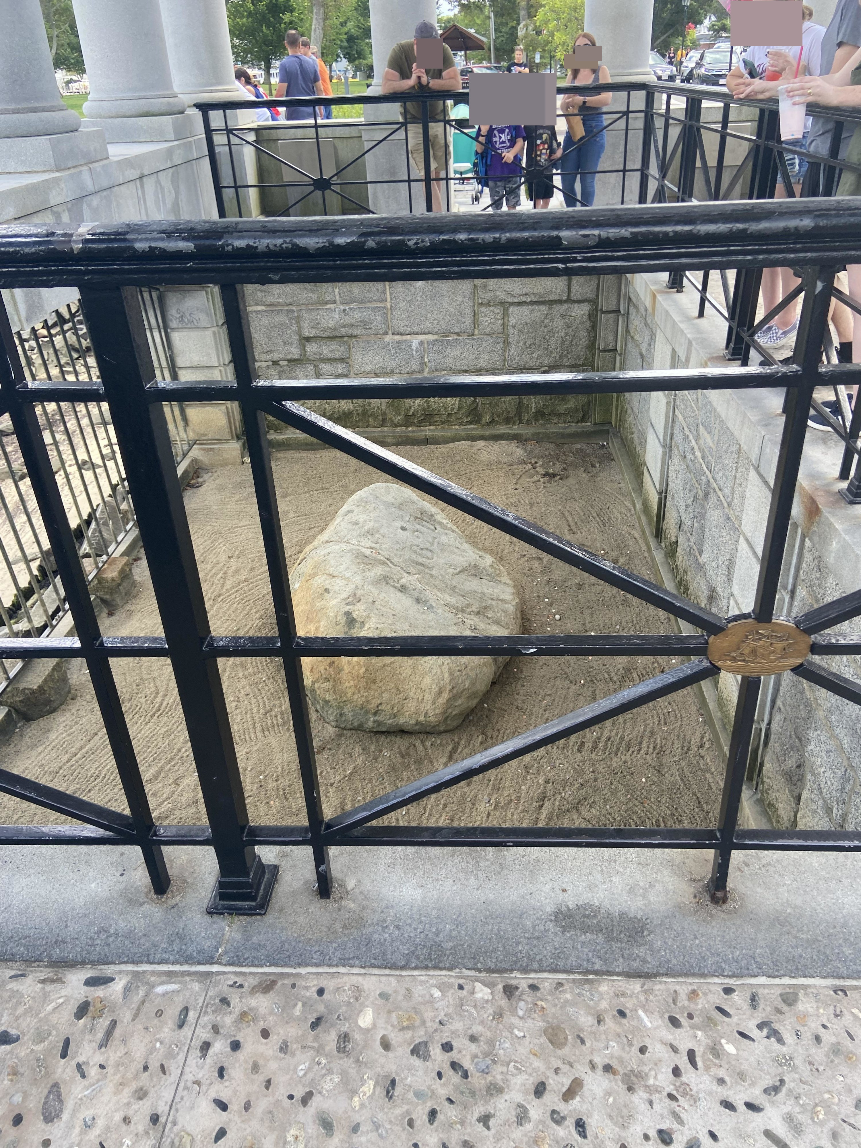 A large but not enormous rock behind bars, with people looking at it