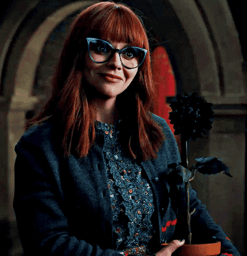 Christina wearing large eyeglasses and smiling as she holds a potted plant