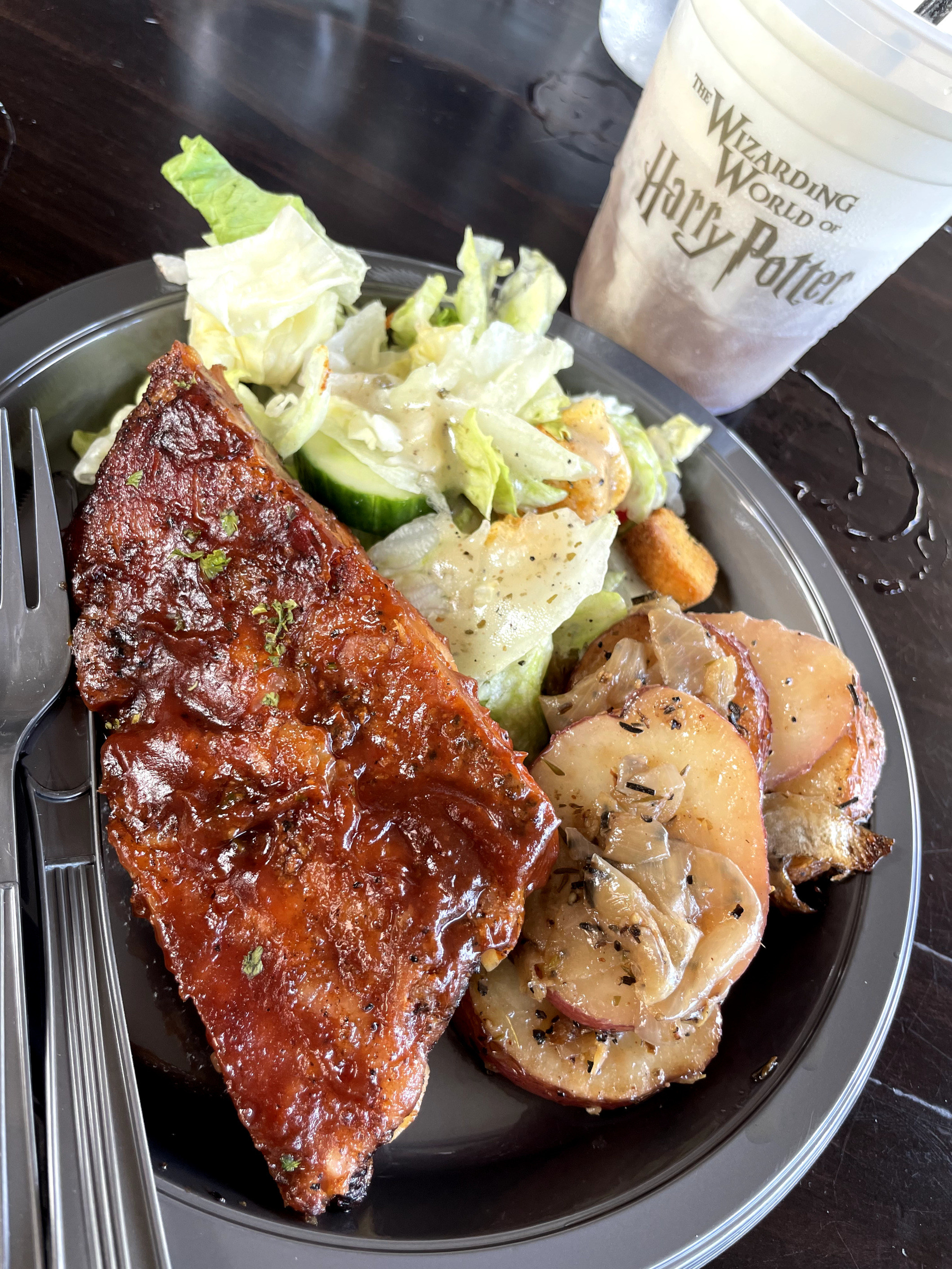 A photo of BBQ ribs, potatoes and salad on a plate with a drink on the side