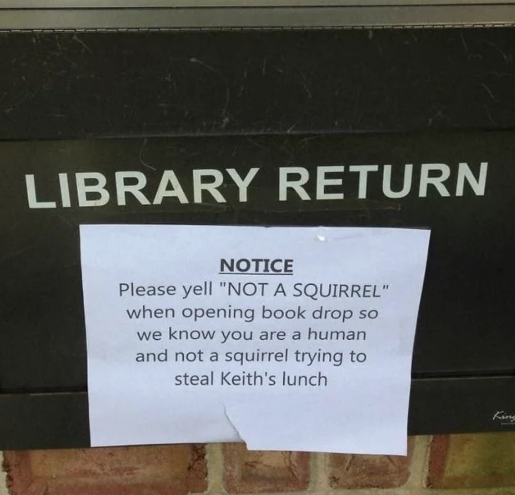 Sign says, Please yell &#x27;NOT A SQUIRREL&#x27; when opening book drop so we know you are a human and not a squirrel trying to steal Keith&#x27;s lunch