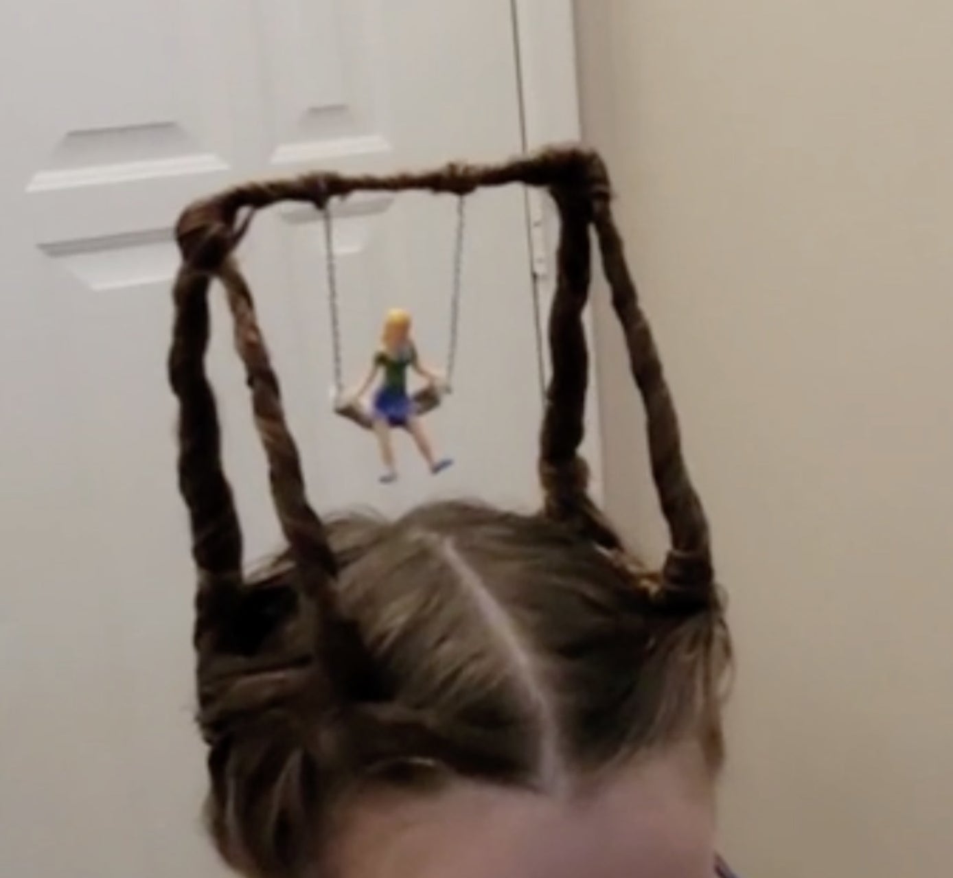 A little girl&#x27;s pigtails forming the frames of a swing from which a doll sits