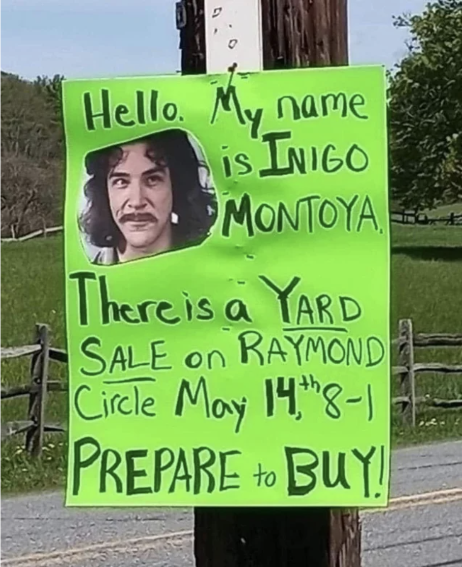 A sign on an outdoor pole — &quot;Hello, my name is Inigo Montoya, there is a yard sale on Raymond Circle, May 14, 8–1, prepare to buy!&quot; — with a photo of Mandy Patinkin as Inigo