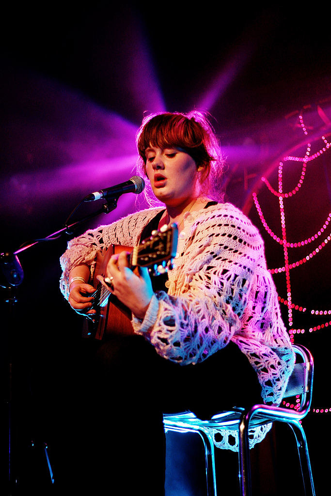 Adele sitting onstage and playing guitar