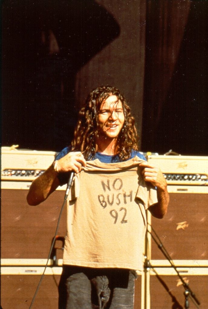 Eddie smiling and holding up a &quot;No Bush 92&quot; T-shirt