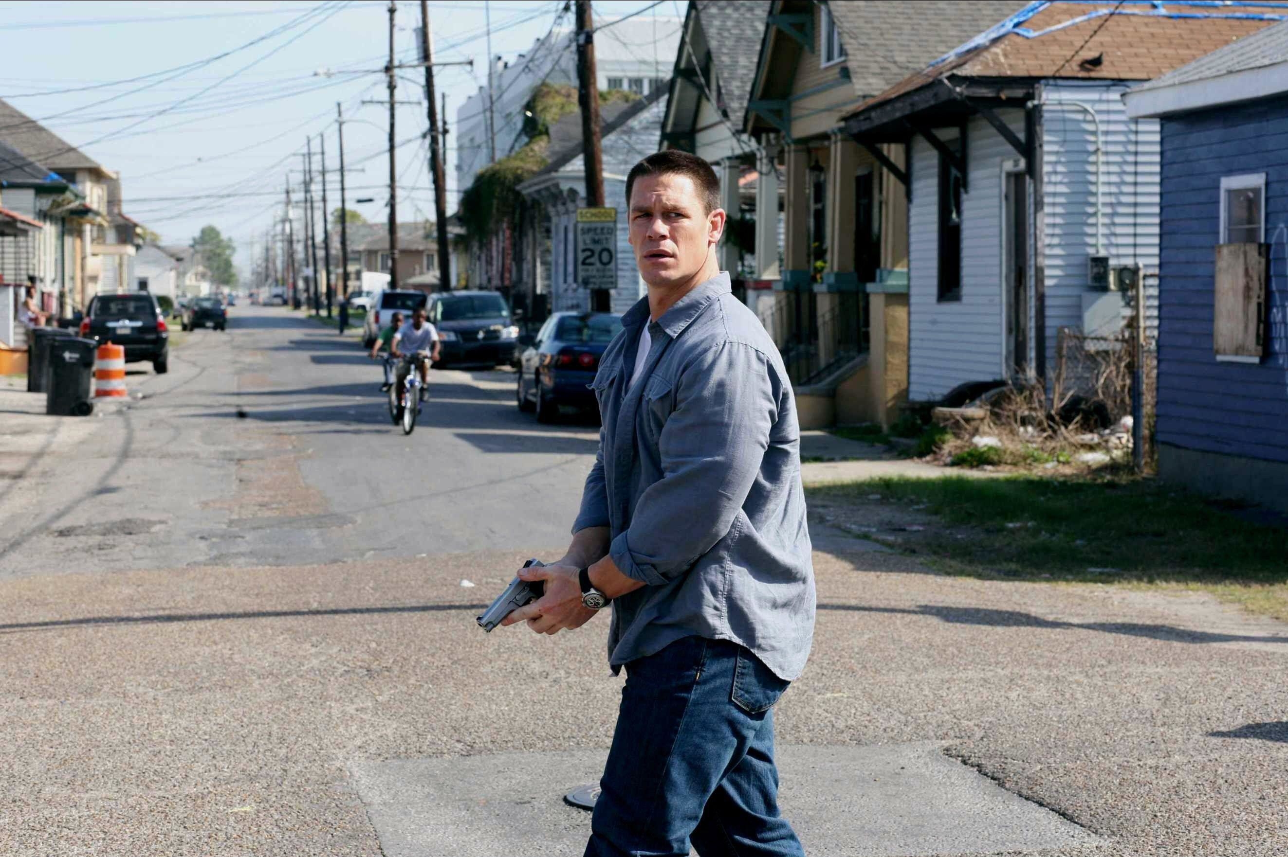 A man with a gun in denim and a button-up shirt stands with concern in the middle of a street