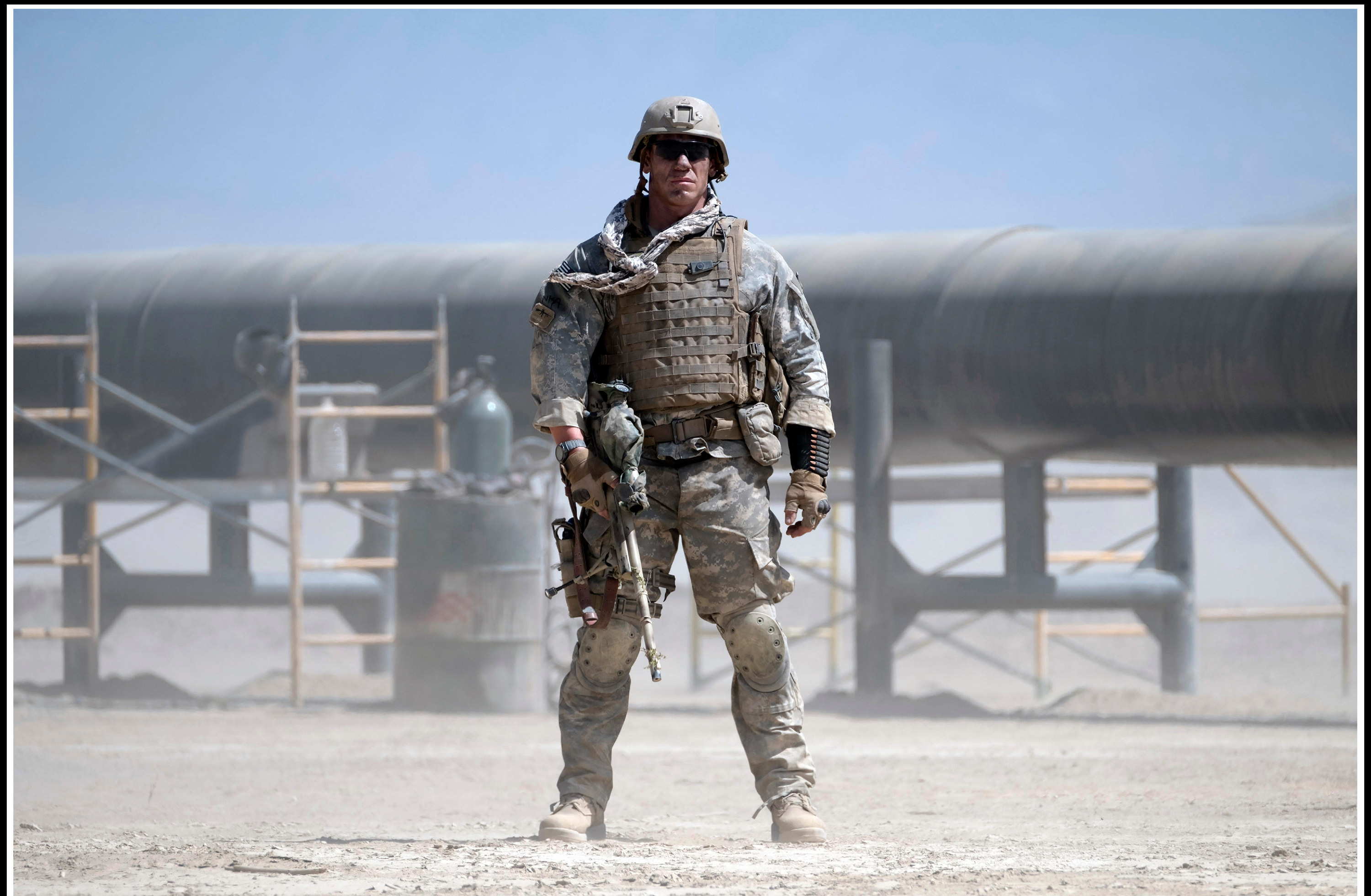 A large American soldier stands ready with gun-in-hand near an oil pipeline