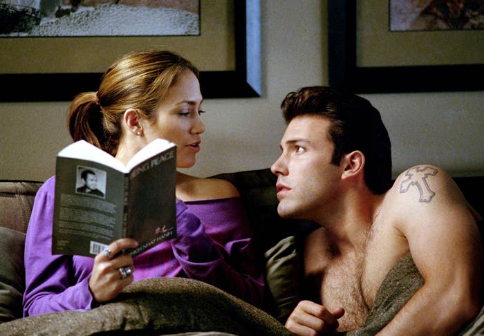 JLo and Ben Affleck in bed looking at each other, as JLo holds a book open