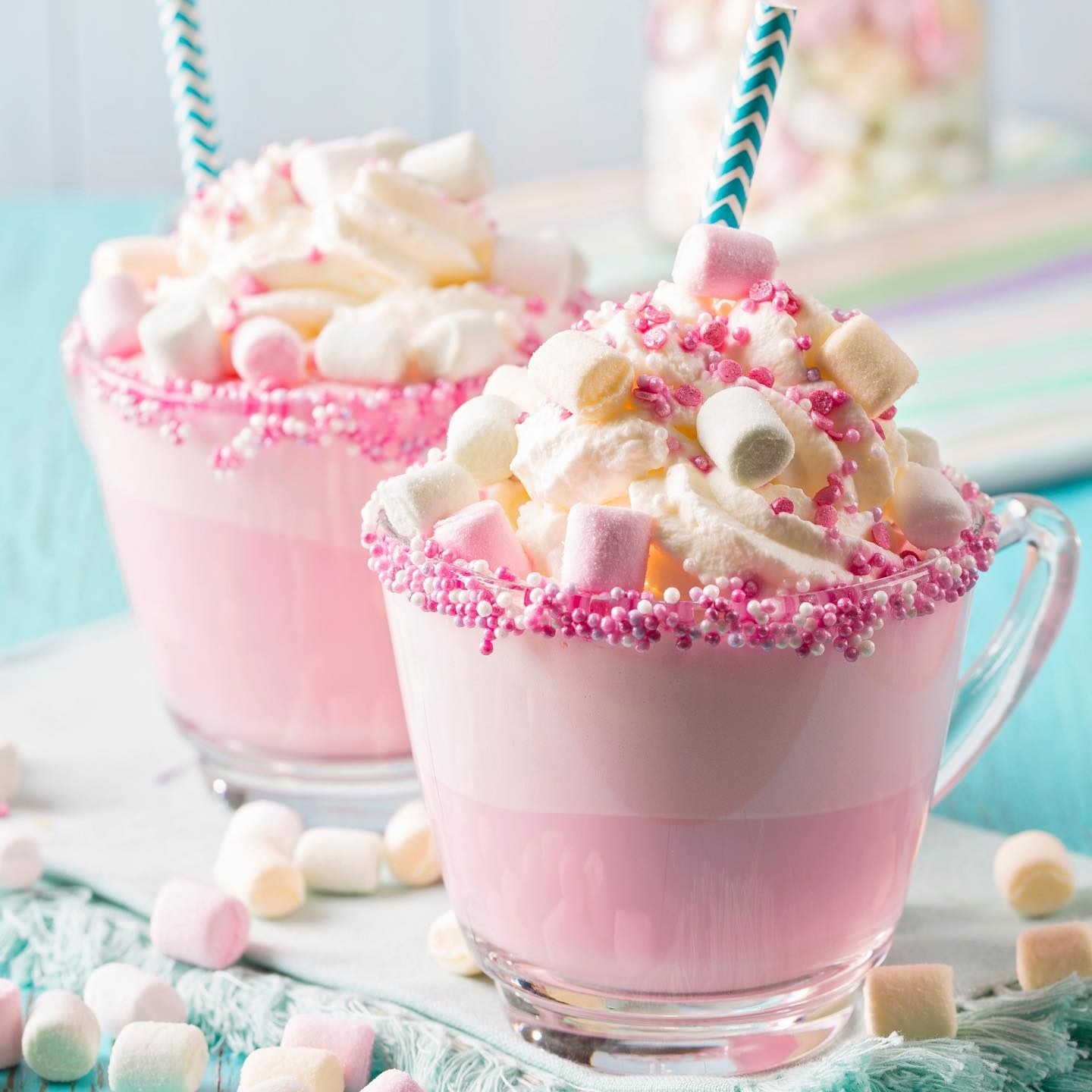 two glass mugs of the cocoa on a table surrounded by mini marshmallows