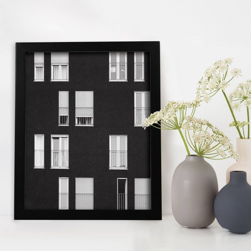 the black frame with a photo of windows in it next to a set of grey and white vases with white flowers