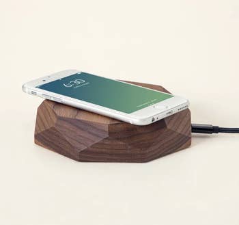 A smartphone resting on a geometric walnut wood charger with a flat top