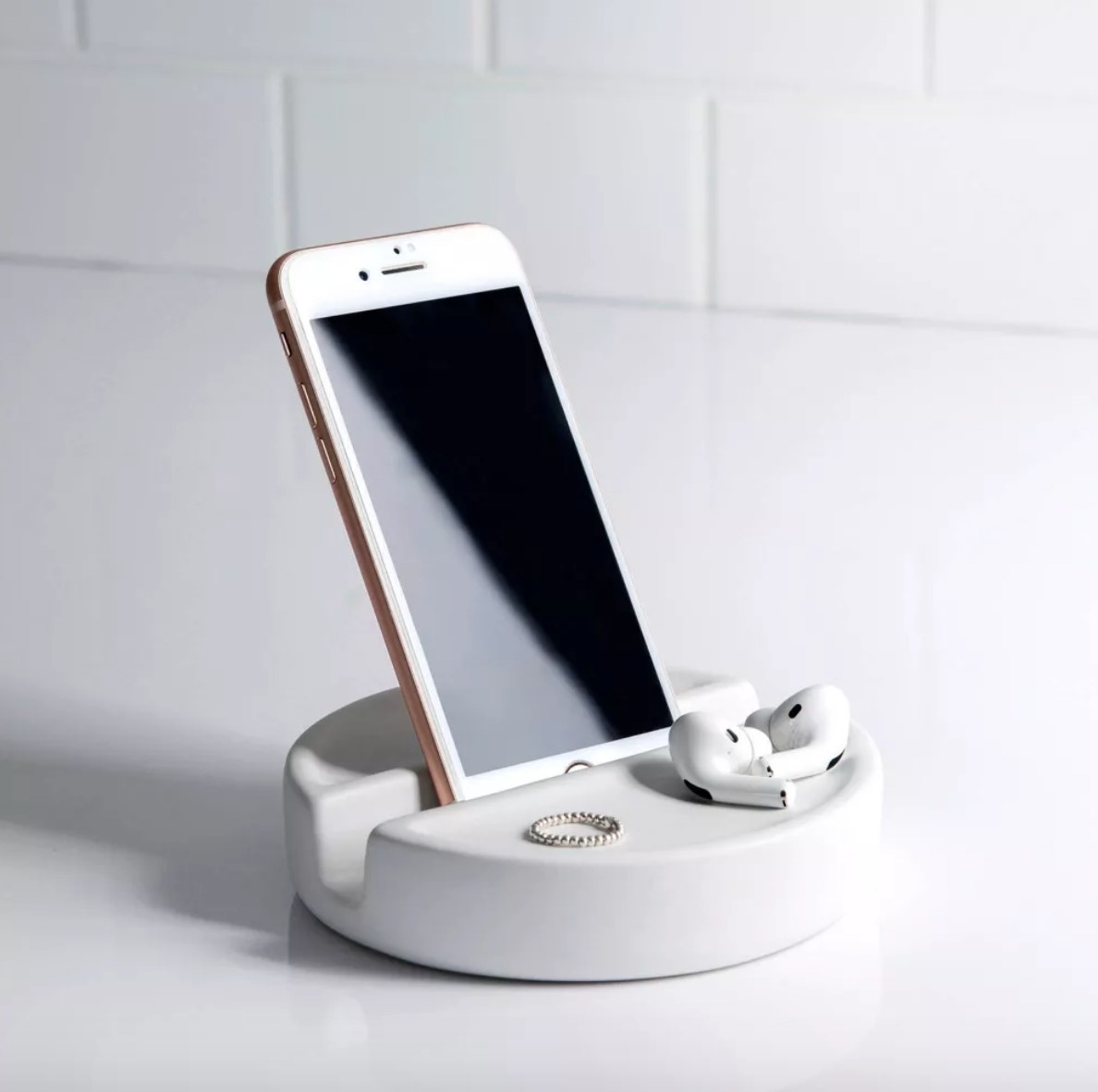 White round cellphone holder holding white cell phone with ring and airpods resting on holder