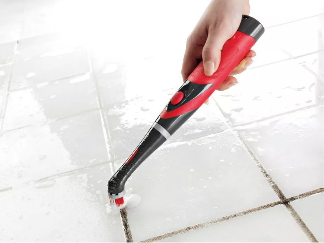 Model using black and red power scrubber on grout of white tiles