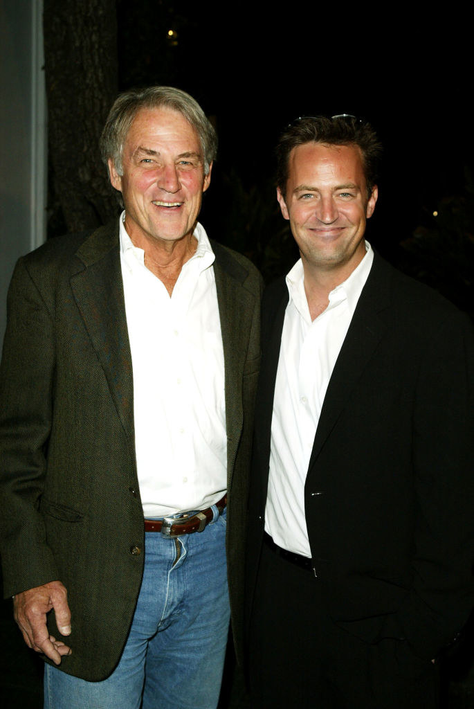An adult Matthew smiling with his dad as they pose for a photograph