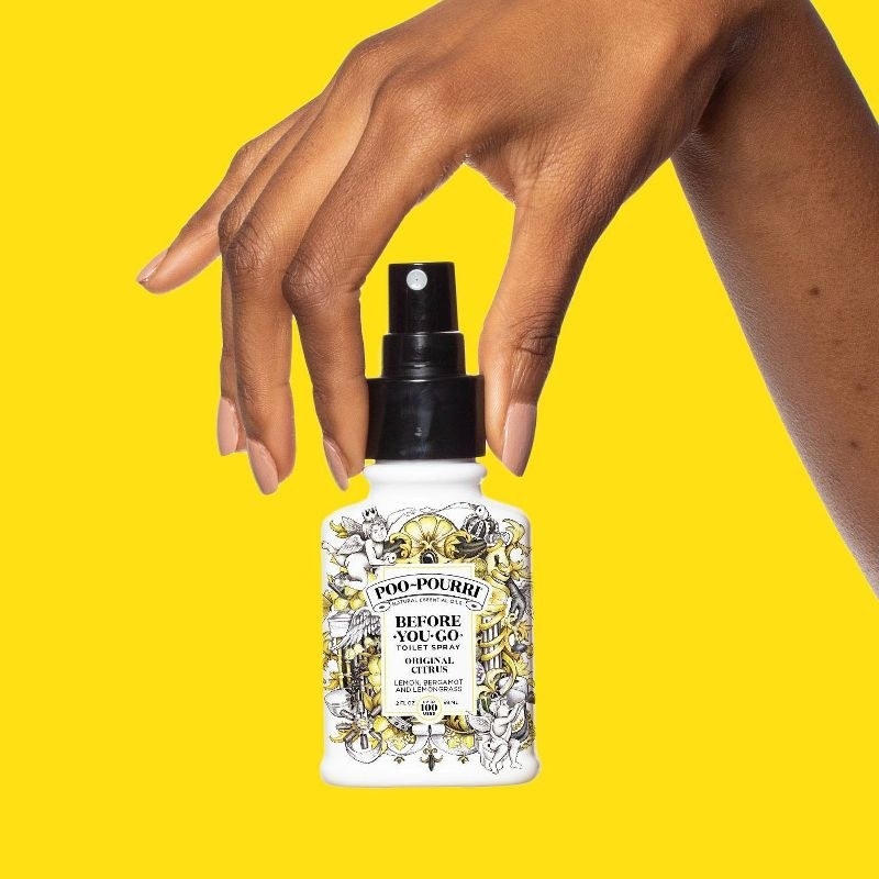 a model holding the black floral spray bottle in front of a yellow background