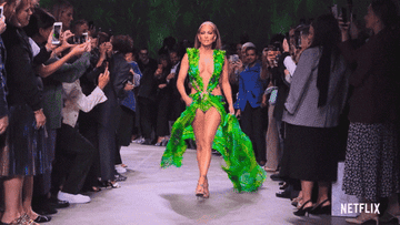 J Lo on a runway opening up her dress sides with people photographing her