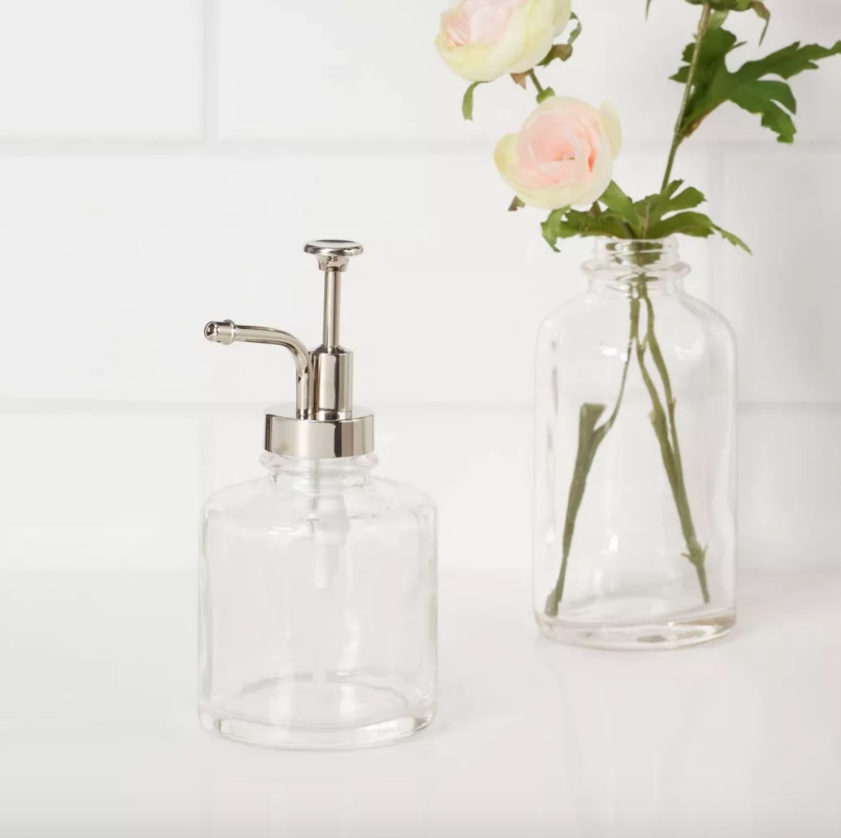Empty glass soap pump on counter next to clear vase of flowers