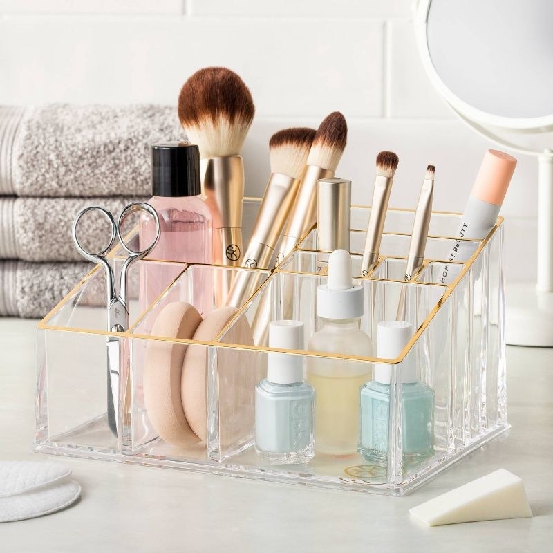 the clear makeup organizer with gold edges filled with products and brushes