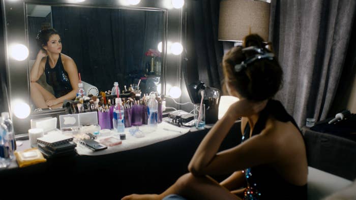 Selena looking into a mirror as she sits in a dressing room