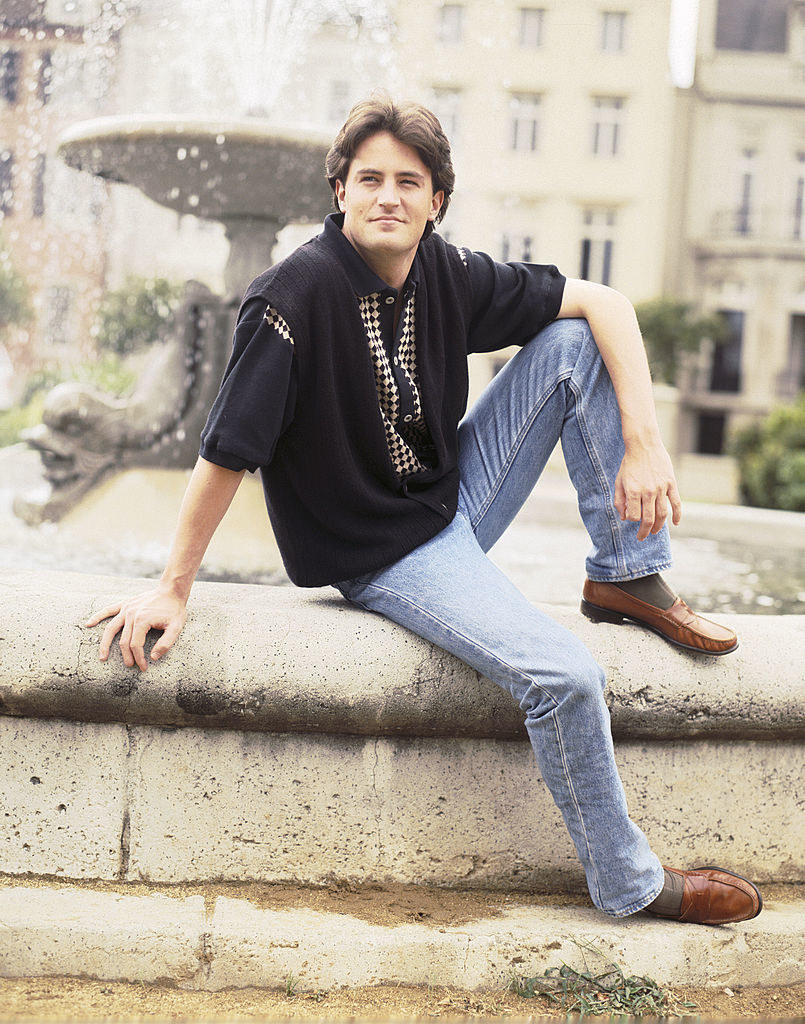 Matthew as Chandler sitting on the ledge of a fountain in a promo photo fro Friends