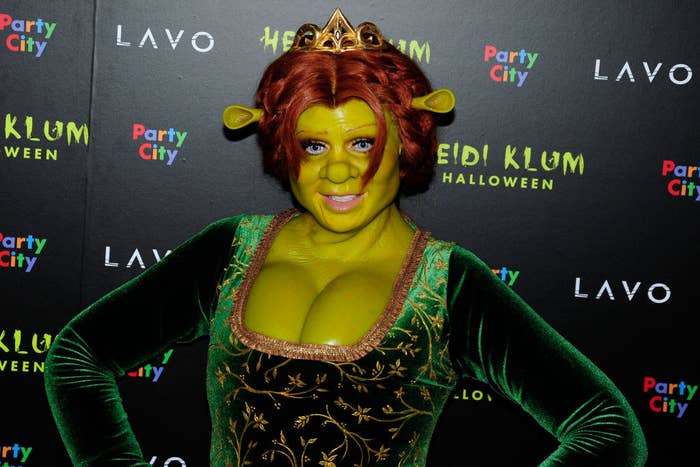 Heidi with small crown and small ears protruding from the side of her head, green skin, a green, bodice-baring velvet dress, and fake bustline