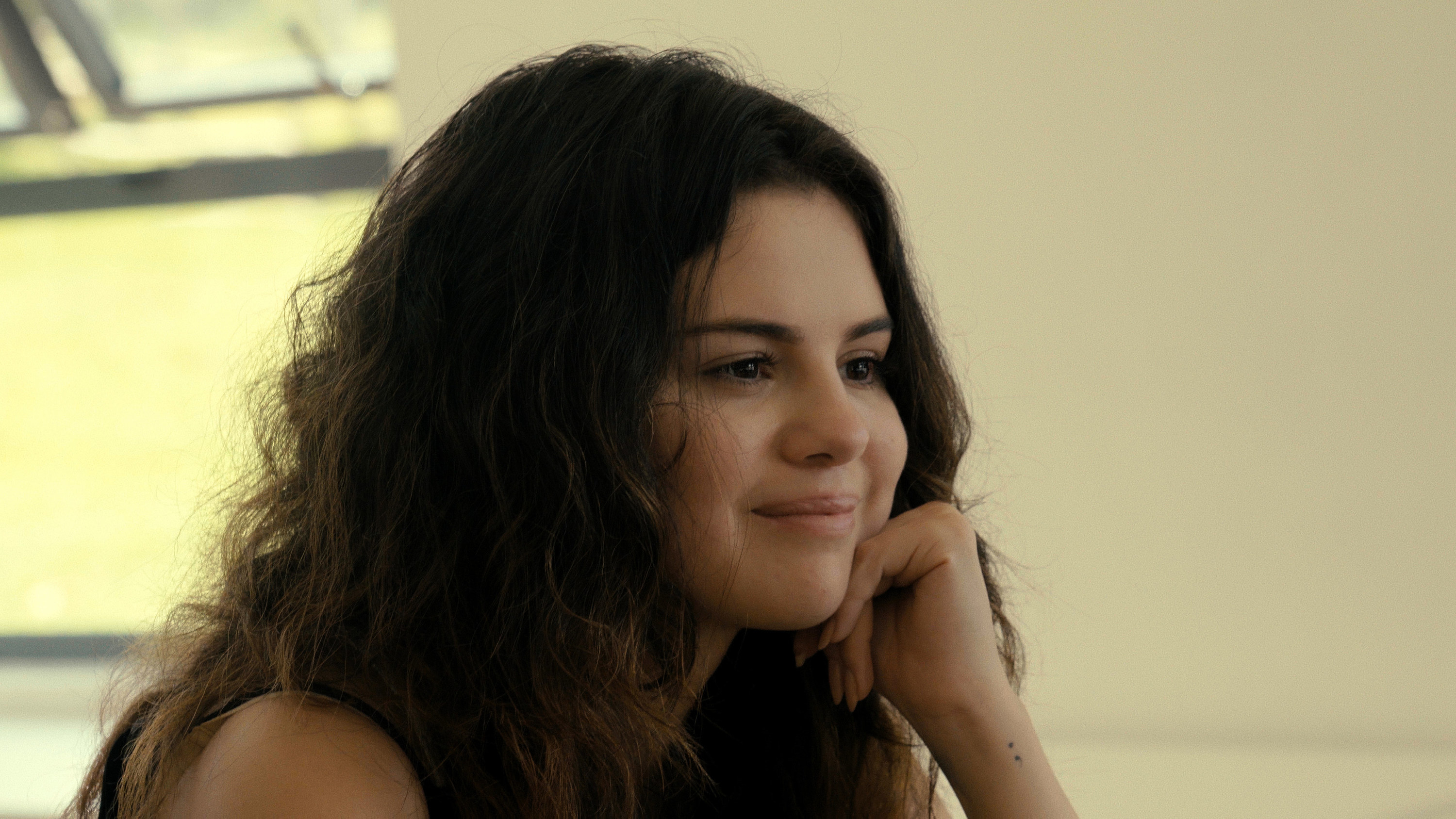 Selena Gomez smiles with her hand near her face